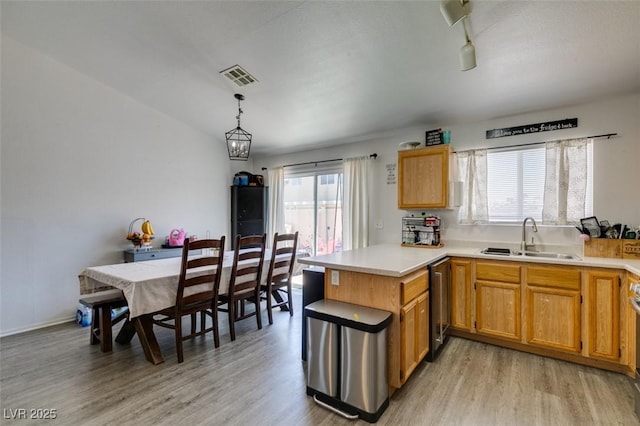 kitchen featuring light countertops, light wood-type flooring, a sink, visible vents, and a peninsula