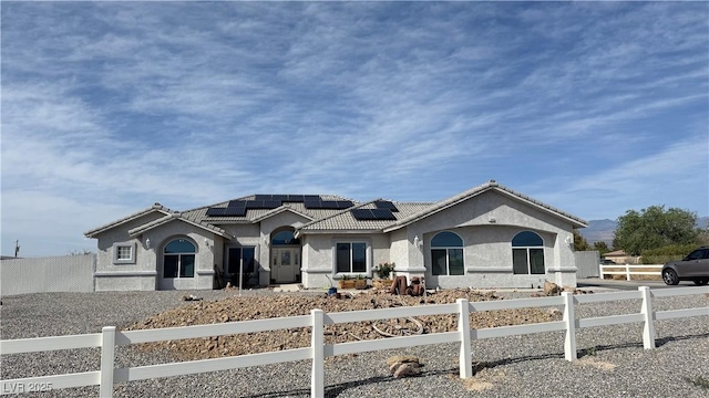 view of front of property with roof mounted solar panels, a tiled roof, stucco siding, and a fenced front yard