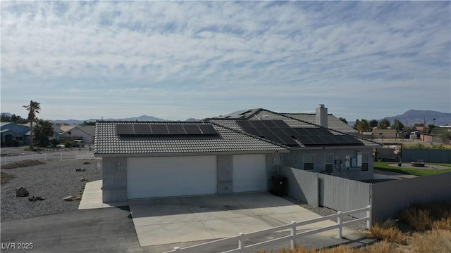 view of front facade featuring a tiled roof, fence, roof mounted solar panels, a mountain view, and an attached garage
