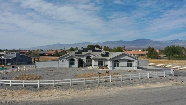 view of front of house with stucco siding, solar panels, a mountain view, and fence private yard