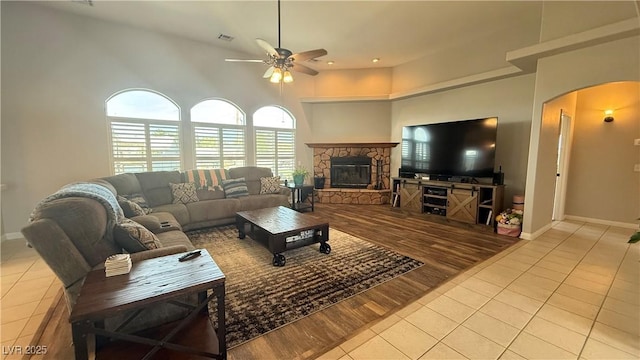 living area with ceiling fan, tile patterned floors, a stone fireplace, baseboards, and arched walkways