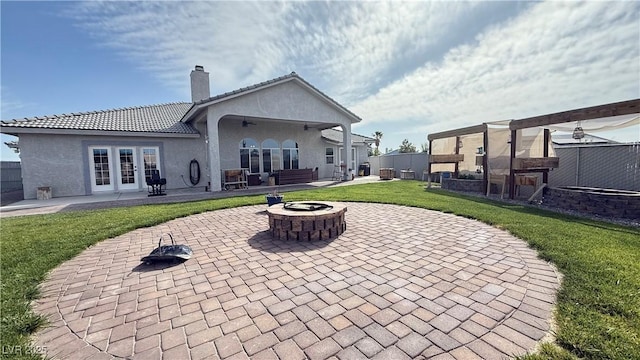 back of property with a patio, a chimney, an outdoor fire pit, a lawn, and french doors