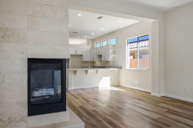 10657 Sapphire Vista Ave, Las Vegas, NV 89144 - unfurnished living room featuring a sink, visible vents, baseboards, a tile fireplace, and wood finished floors