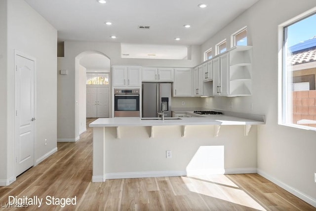 10657 Sapphire Vista Ave, Las Vegas, NV 89144 - kitchen with stainless steel appliances, light wood-style floors, a breakfast bar, a peninsula, and arched walkways