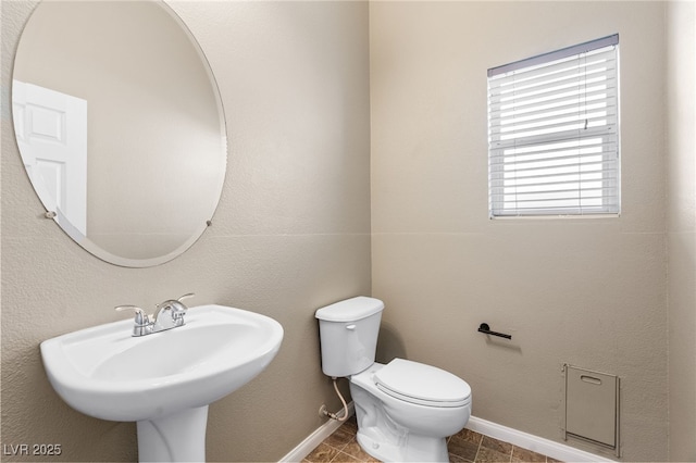 bathroom featuring baseboards, toilet, and a sink