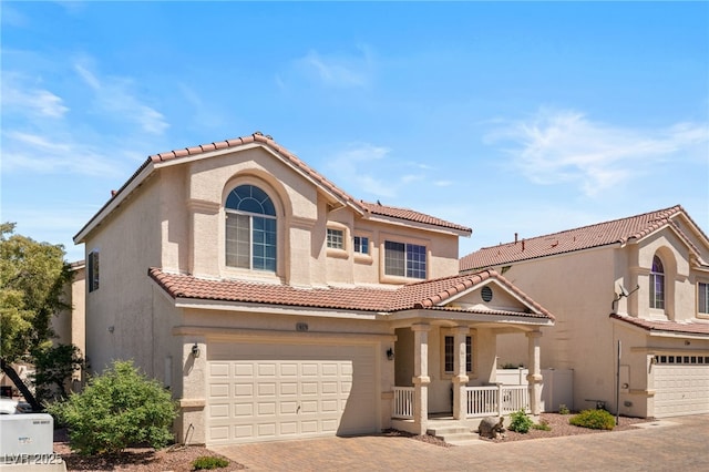 mediterranean / spanish house featuring a porch, stucco siding, decorative driveway, a tiled roof, and an attached garage