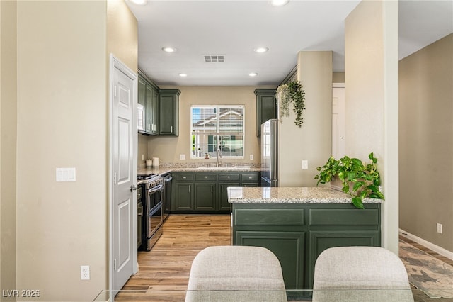 kitchen featuring green cabinetry, visible vents, stainless steel appliances, light stone countertops, and recessed lighting
