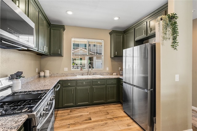 kitchen with light wood-style flooring, appliances with stainless steel finishes, green cabinets, and a sink