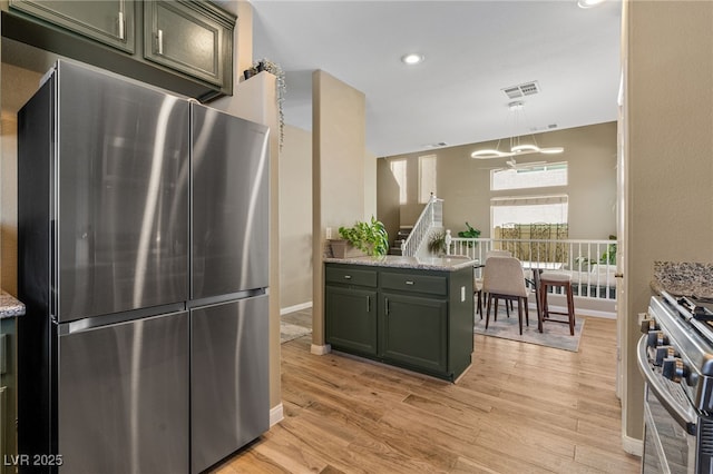 kitchen with light stone counters, green cabinetry, appliances with stainless steel finishes, light wood-type flooring, and visible vents