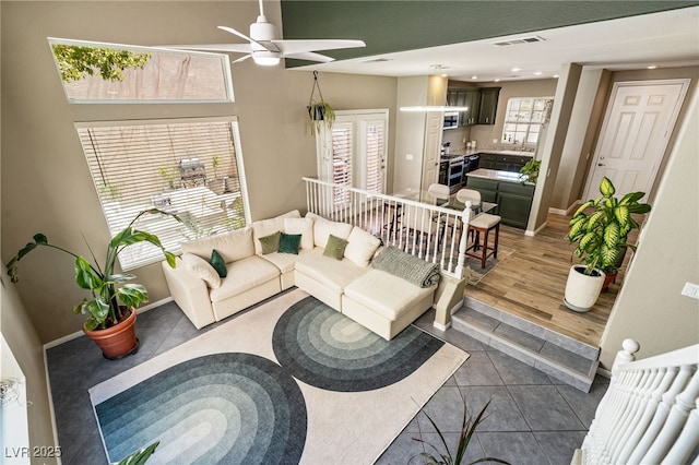 living area with tile patterned flooring, visible vents, ceiling fan, and baseboards