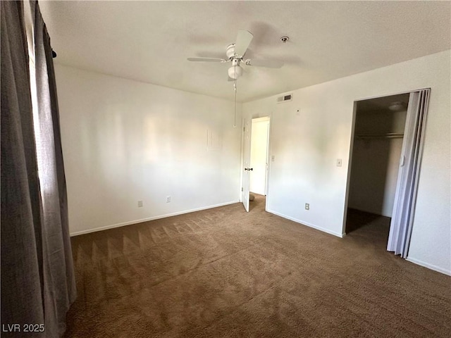 unfurnished bedroom with a closet, ceiling fan, baseboards, a spacious closet, and dark carpet