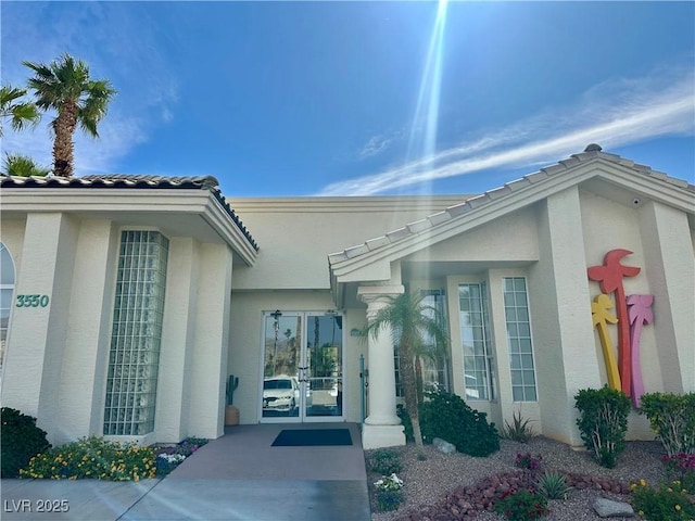 entrance to property featuring stucco siding, french doors, and a tiled roof