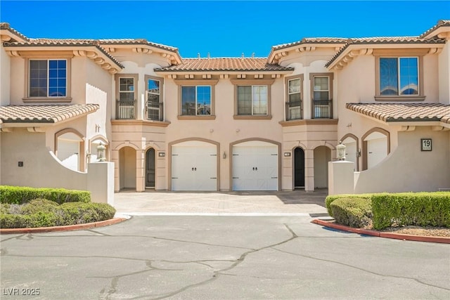 view of front facade with stucco siding, a balcony, a tiled roof, and an attached garage