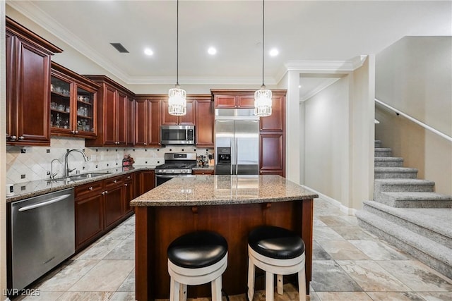 kitchen featuring light stone counters, reddish brown cabinets, a sink, and appliances with stainless steel finishes