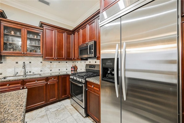 kitchen with light stone countertops, stainless steel appliances, backsplash, a sink, and crown molding