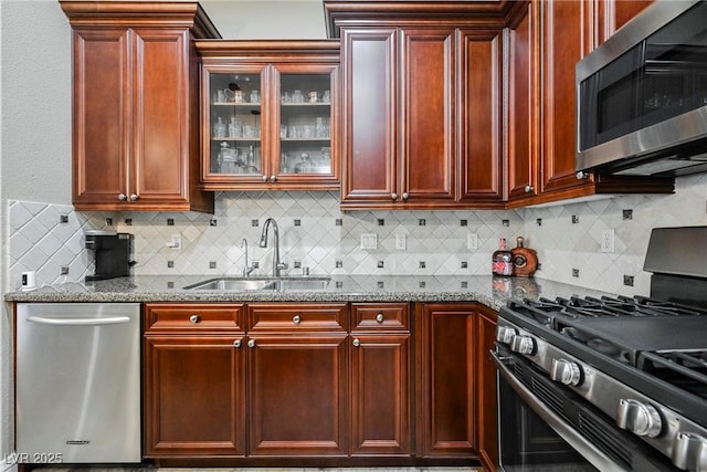 kitchen featuring dark stone countertops, reddish brown cabinets, stainless steel appliances, and a sink