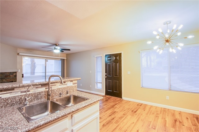 kitchen with white cabinets, a sink, baseboards, light wood-type flooring, and ceiling fan with notable chandelier