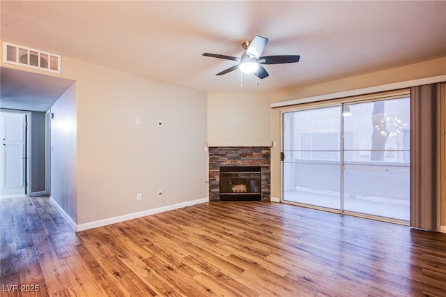 unfurnished living room with wood finished floors, a fireplace, baseboards, visible vents, and a ceiling fan