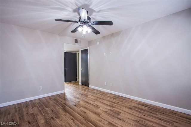 spare room with a ceiling fan, visible vents, wood finished floors, and baseboards