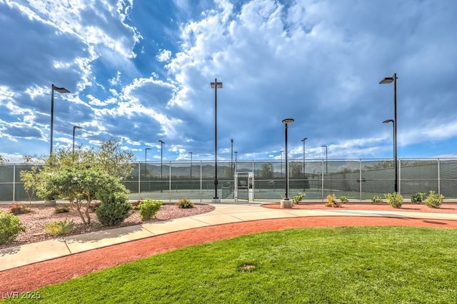 view of tennis court featuring fence and a yard