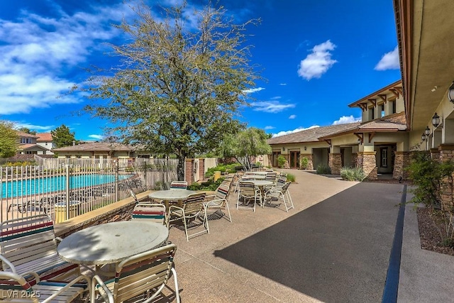 view of patio with fence, outdoor dining area, and a community pool