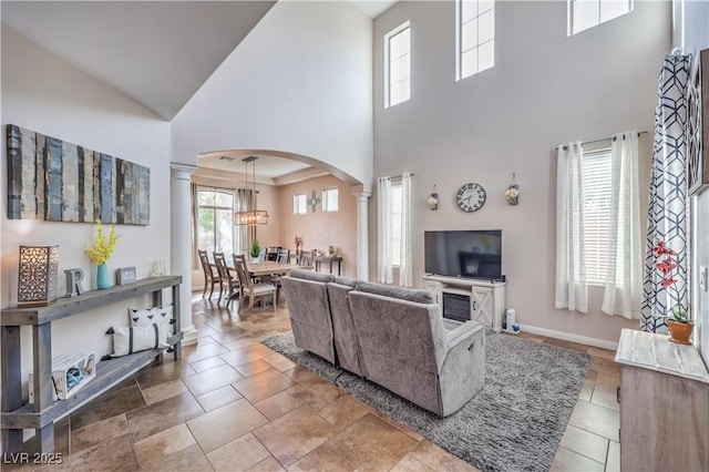 living area with ornate columns, baseboards, arched walkways, and a high ceiling
