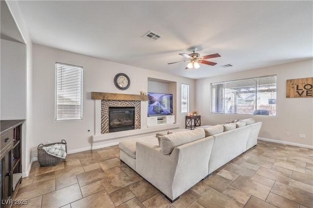 living area featuring a tiled fireplace, stone finish flooring, a ceiling fan, visible vents, and baseboards