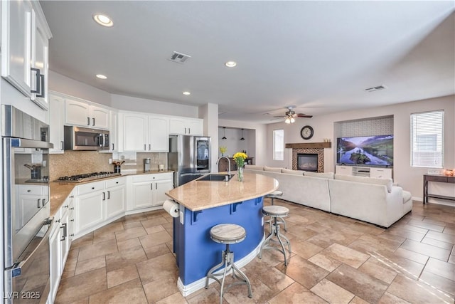kitchen featuring light stone countertops, a sink, stainless steel appliances, decorative backsplash, and open floor plan