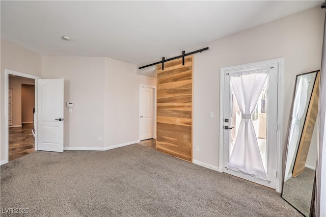 carpeted spare room with a barn door and baseboards