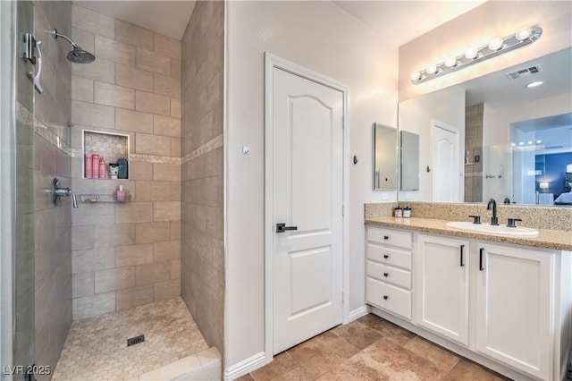 full bath with a tile shower, visible vents, vanity, and baseboards