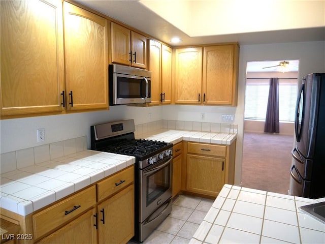 6508 Alpine Forest Ct, Las Vegas, NV 89149 - kitchen featuring appliances with stainless steel finishes, tile countertops, light carpet, ceiling fan, and light tile patterned floors