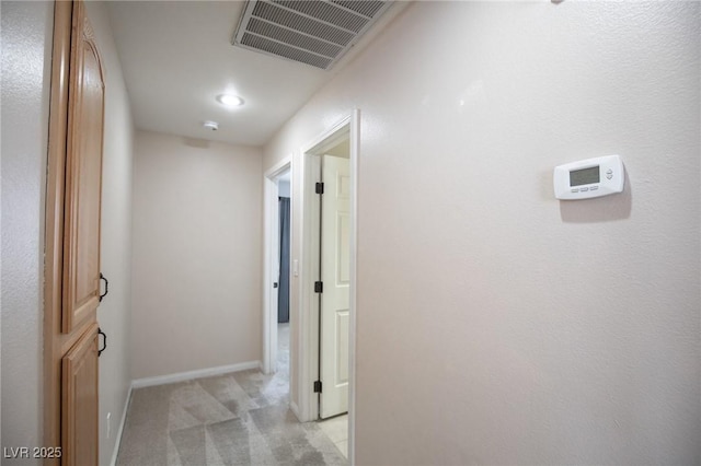 corridor with visible vents, light colored carpet, and baseboards