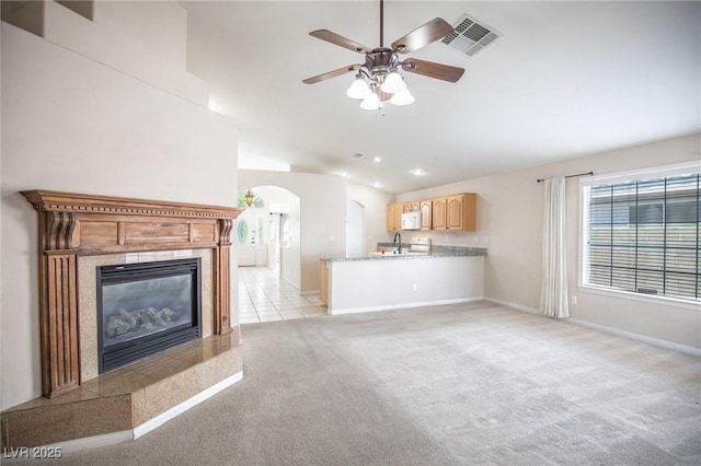unfurnished living room with light colored carpet, visible vents, ceiling fan, arched walkways, and vaulted ceiling
