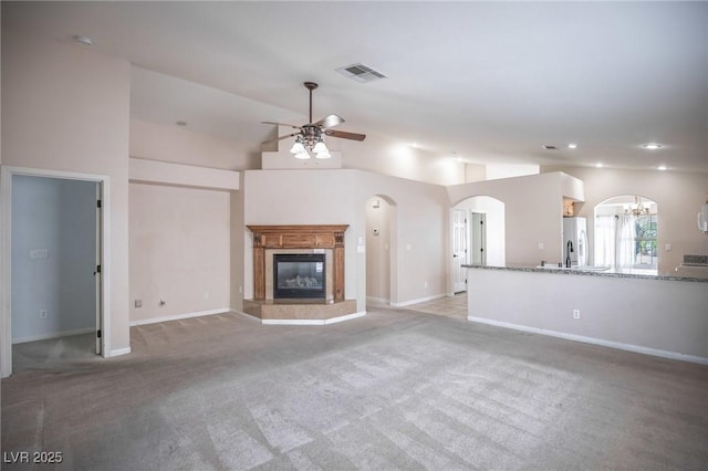unfurnished living room featuring a glass covered fireplace, visible vents, light carpet, arched walkways, and ceiling fan with notable chandelier