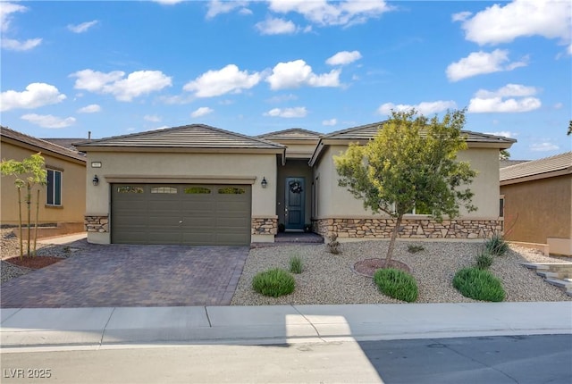 prairie-style house with decorative driveway, stone siding, stucco siding, and an attached garage