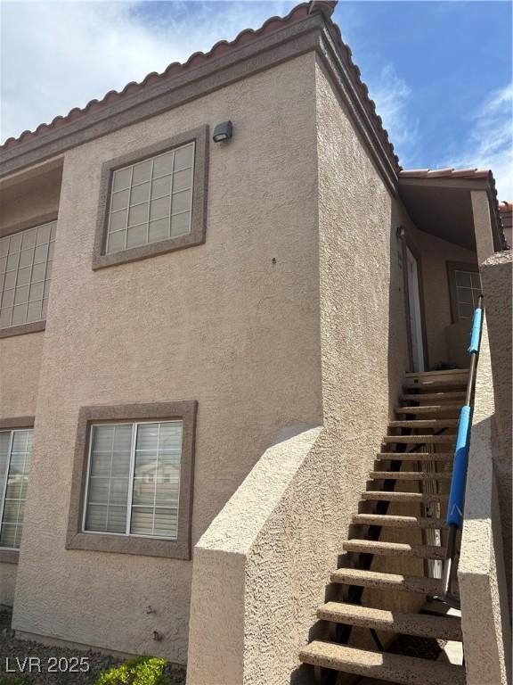 view of property exterior featuring a tile roof, stairs, and stucco siding