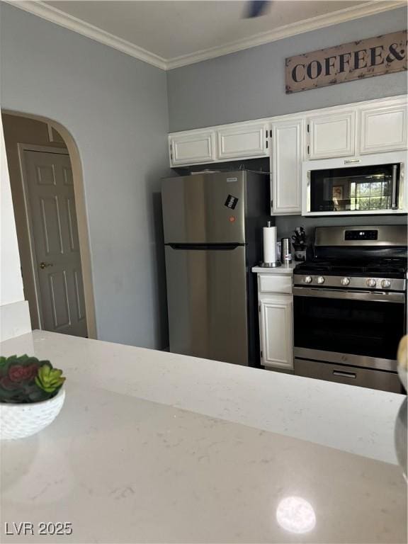 kitchen with arched walkways, light stone counters, appliances with stainless steel finishes, white cabinets, and crown molding