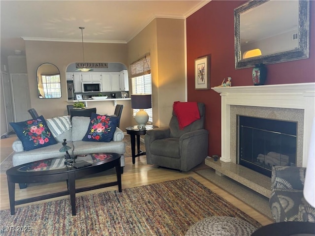 living room with ornamental molding, wood finished floors, and a glass covered fireplace