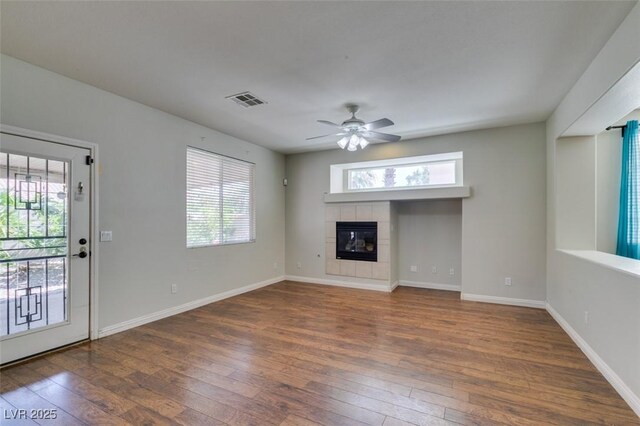 1048 Painted Daisy Ave, Henderson, NV 89074 - unfurnished living room featuring dark wood-style flooring, healthy amount of natural light, ceiling fan, and a tiled fireplace