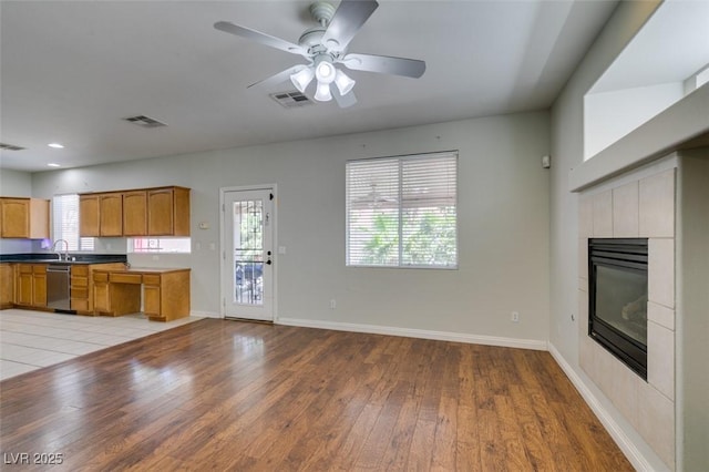 1048 Painted Daisy Ave, Henderson, NV 89074 - kitchen featuring dishwasher, light wood-style flooring, a fireplace, a ceiling fan, and brown cabinetry