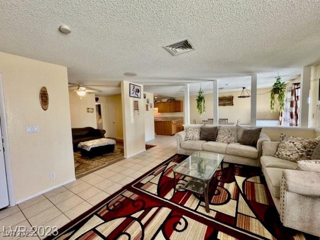 living area with light tile patterned flooring, a textured ceiling, visible vents, and a ceiling fan