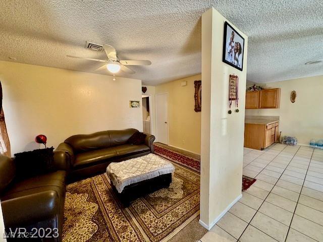 living area featuring visible vents, light tile patterned floors, ceiling fan, and a textured ceiling