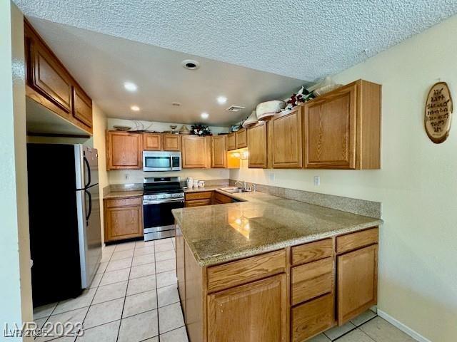 kitchen with a sink, appliances with stainless steel finishes, light tile patterned flooring, recessed lighting, and a peninsula