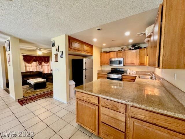 kitchen featuring a sink, light tile patterned floors, a peninsula, a textured ceiling, and appliances with stainless steel finishes