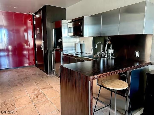 kitchen with stainless steel microwave, a sink, dark countertops, a peninsula, and backsplash