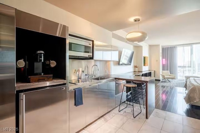 kitchen featuring decorative light fixtures, appliances with stainless steel finishes, a sink, open floor plan, and modern cabinets