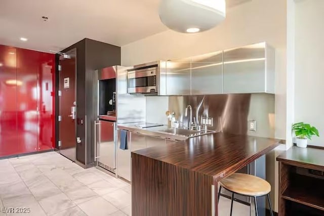 kitchen featuring a breakfast bar area, a sink, marble finish floor, and stainless steel microwave