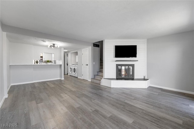 unfurnished living room with wood finished floors, a large fireplace, stairs, and baseboards