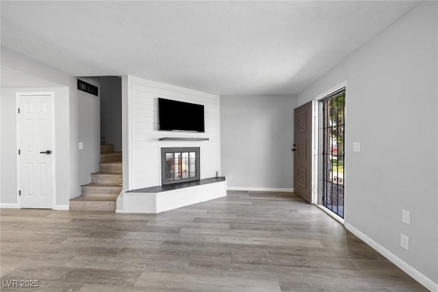 unfurnished living room featuring a large fireplace, visible vents, stairs, and baseboards