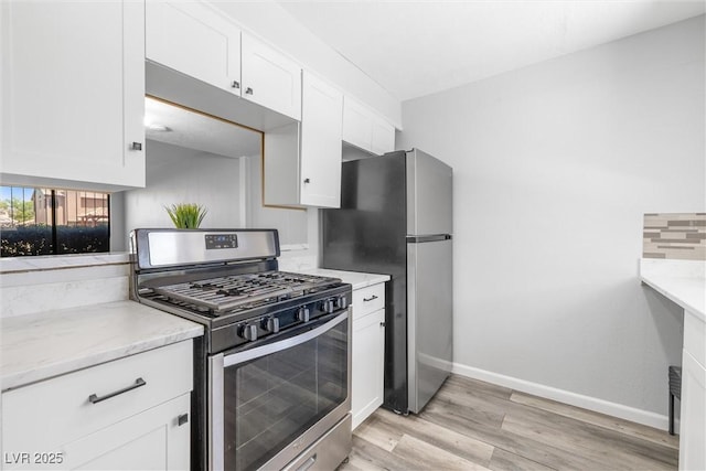 kitchen with baseboards, light stone countertops, stainless steel appliances, light wood finished floors, and white cabinetry